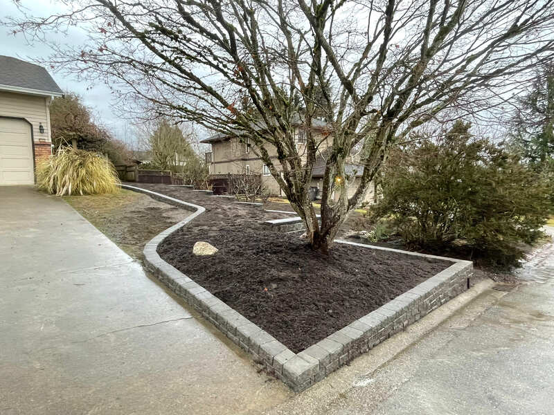 showing the stack stone follow along hte driveway then up the lawn parallel to the allan block wall . the entire area is filled with mulch
