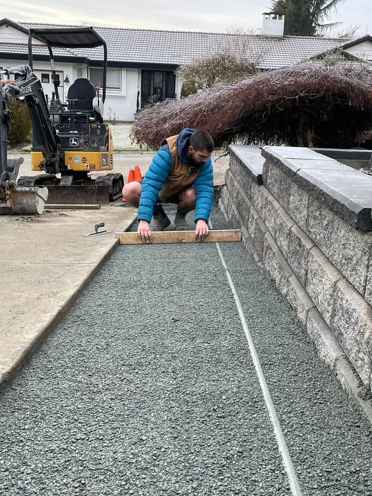 atkinson landscaping foreman screeding the crusher fines with a 2x4 preparing it for pavers to be layed
